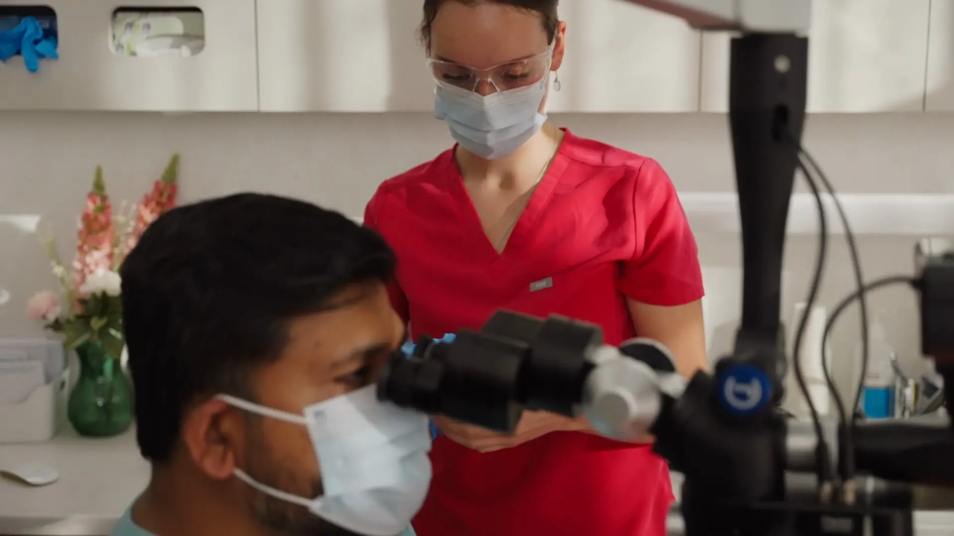 A dentist working through the microscope with an assistant behind