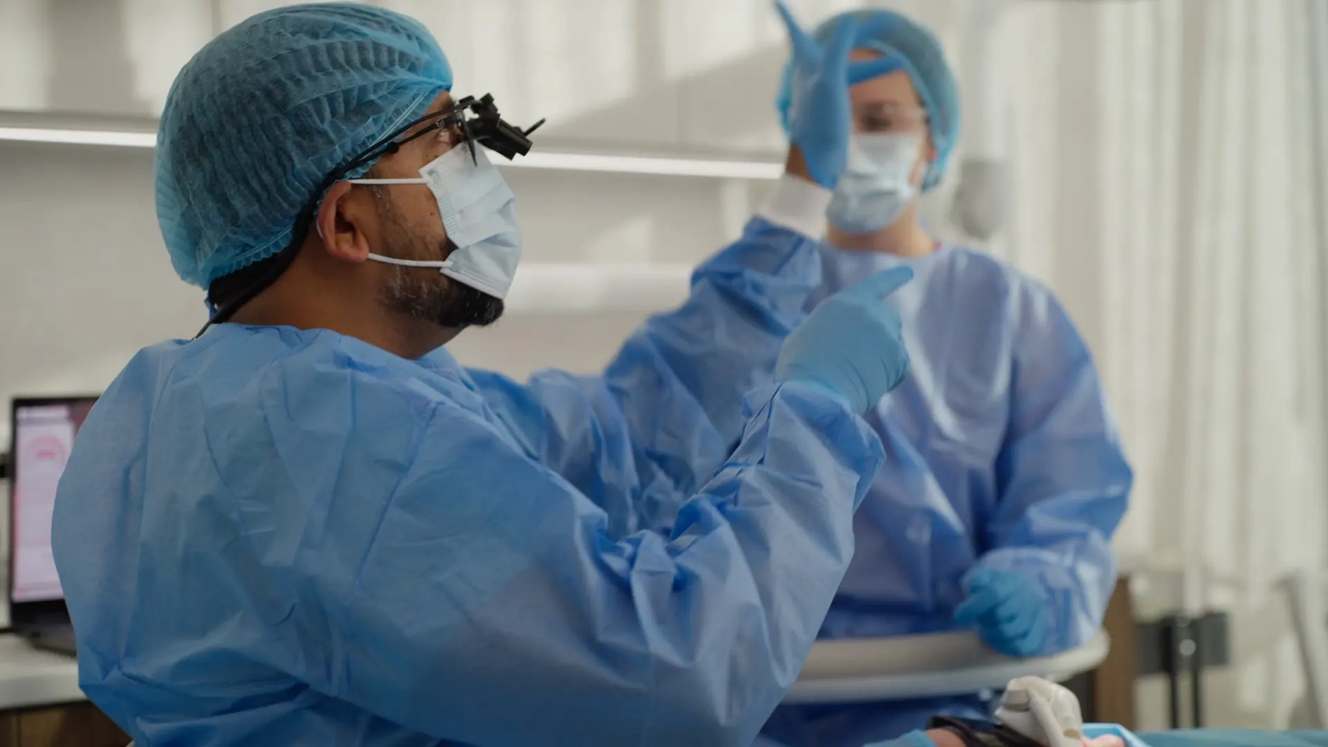 A dentist and assistant in surgical gowns preparing for a sedation appointment